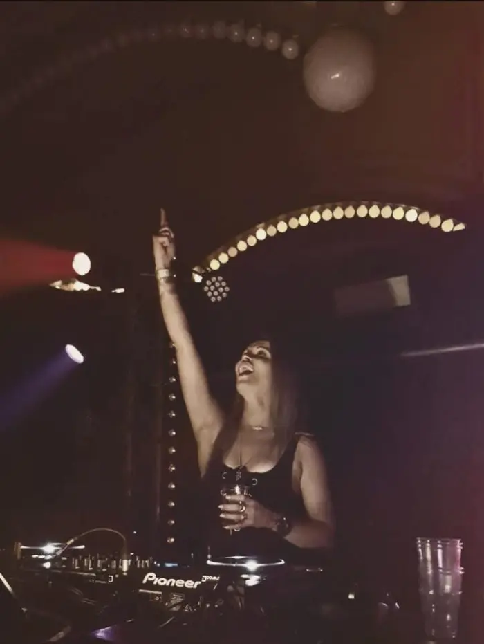 Adrelina pointing up in a dark club under a ring of lights