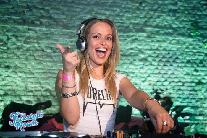 Adrelina in an Adrelina shirt, laughing and pointing behind the decks